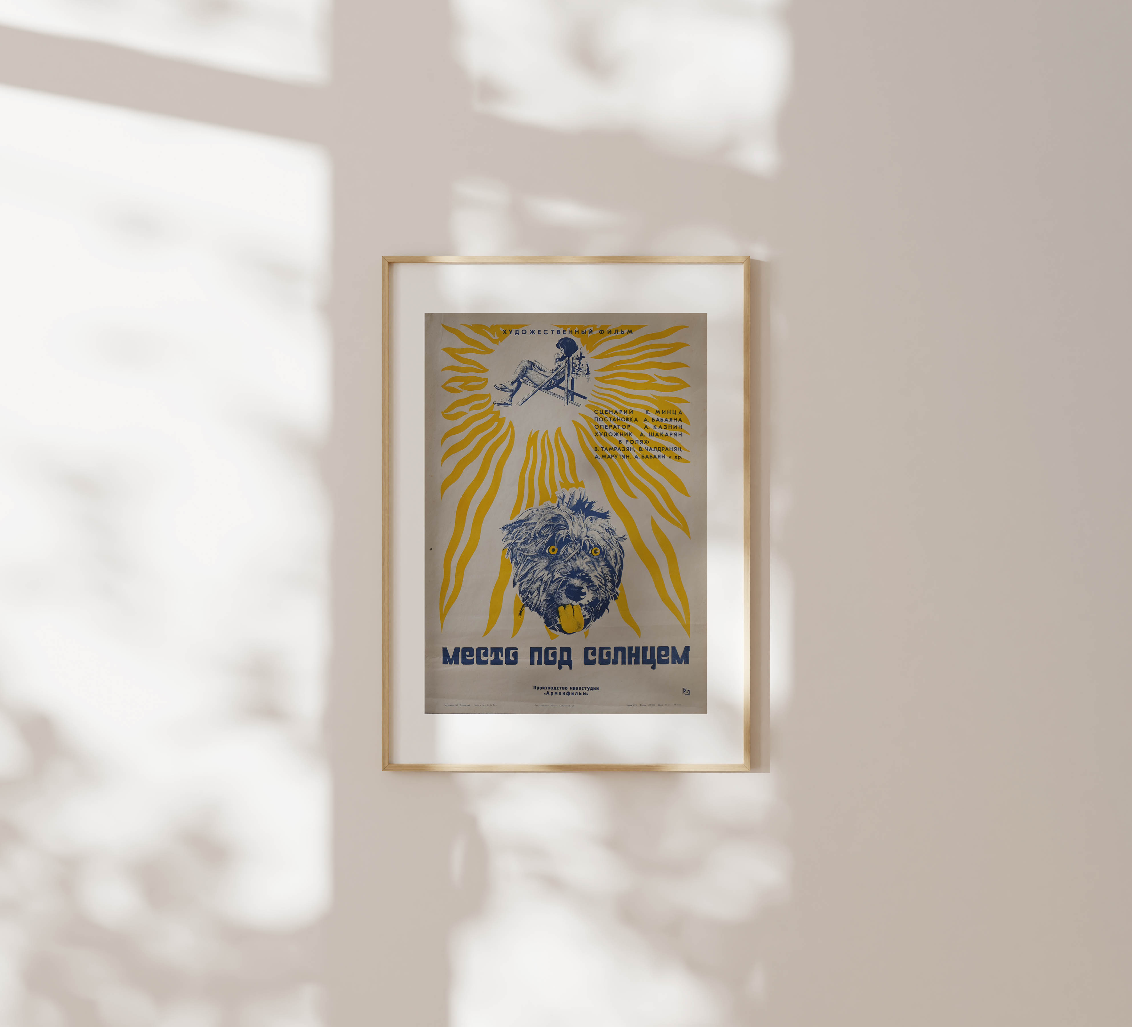 Framed Soviet movie poster featuring a blue shaggy dog and a stylized yellow sun, hanging on a minimalist beige wall with delicate leaf shadows.