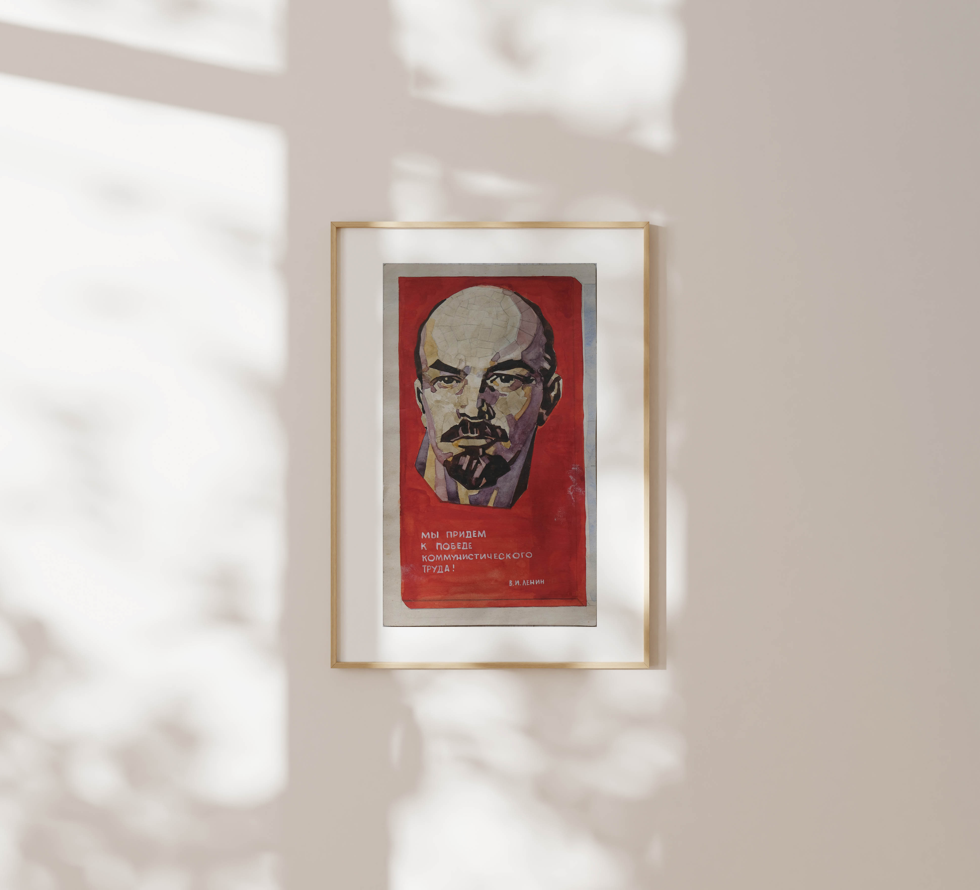 Framed watercolour portrait of Lenin hanging on a light cream wall, dappled with soft natural shadows from leaves.